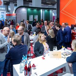 Am Stand des Börsenvereins auf der Frankfurter Buchmesse 2025 stehen viele Menschen, die sich in Gruppen miteinander unterhalten. Die meisten stehen, ein paar sitzen an erhöhten Tischen.