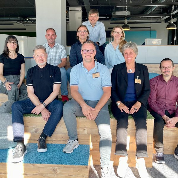 Neun Personen sitzen auf einer mehrstufigen Empore beieinander. Die Personen sind Teilnehmende der Sitzung der Kommission Medienproduktion der Deutschen Fachpresse.